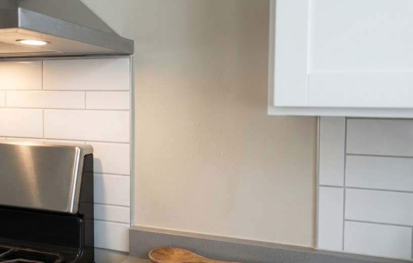 Water droplets beading on a kitchen wall beside a range hood and tile backsplash