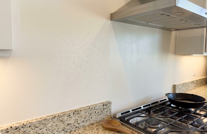 grease spatter on a white kitchen wall beside a stove and range hood
