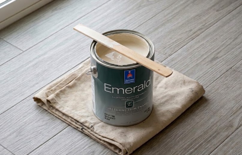 Peach Painting - How to Get Rid of Paint Smell Fast in Tampa: Move the Air Out Open gallon of off-white paint with a wooden stir stick across the top, sitting on a folded canvas drop cloth on a wood-look tile floor