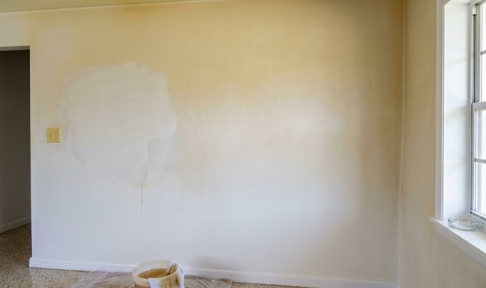 Yellowed wall with a lighter section showing smoke residue, with a cleaning bucket and sponge on the floor