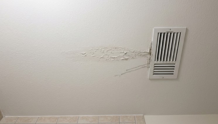 Cracked paint and drip lines spreading from an air conditioning vent on a bathroom ceiling