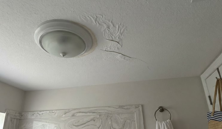 Wrinkled, cracking paint beside a ceiling light fixture in a bathroom
